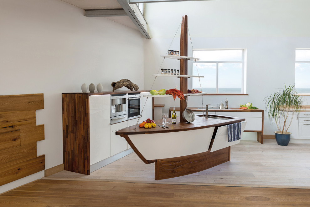 This is an example of a coastal kitchen in Devon with a submerged sink, flat-panel cabinets, white cabinets, wood worktops, stainless steel appliances, light hardwood flooring and an island.