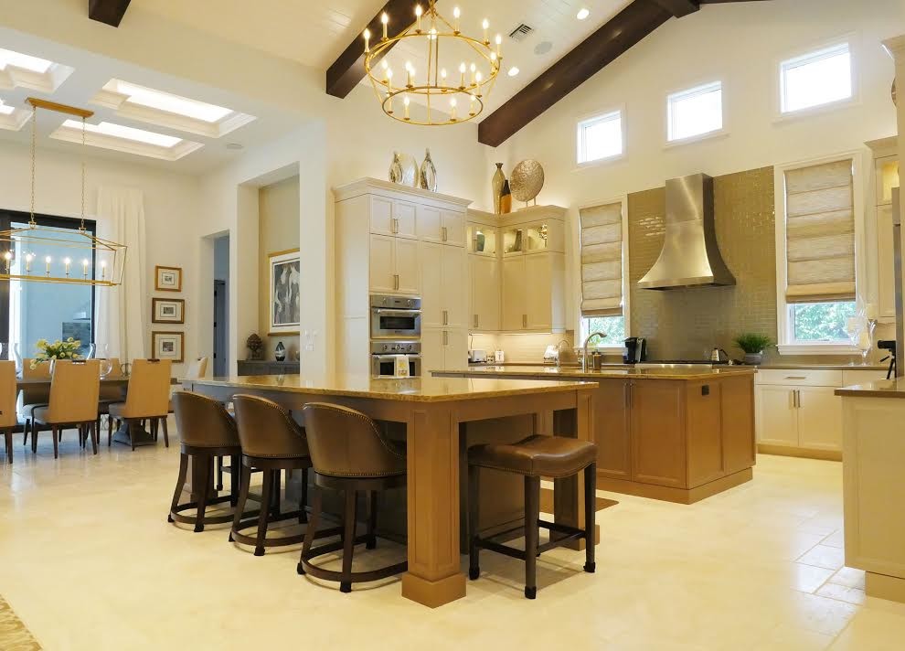 Example of a mid-sized transitional u-shaped travertine floor and beige floor kitchen design in Miami with recessed-panel cabinets, beige cabinets, brown backsplash, glass tile backsplash, stainless steel appliances and two islands