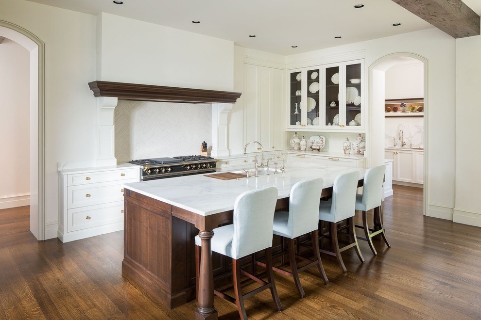 Foto på ett medelhavsstil l-kök, med en undermonterad diskho, luckor med glaspanel, vita skåp, vitt stänkskydd, mellanmörkt trägolv och en köksö