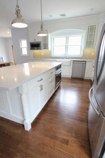 Inredning av ett klassiskt mellanstort kök, med en rustik diskho, luckor med infälld panel, vita skåp, bänkskiva i kvartsit, grått stänkskydd, stänkskydd i keramik, rostfria vitvaror, en köksö, brunt golv och mörkt trägolv