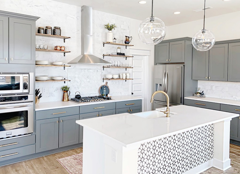 Inspiration for a modern l-shaped open plan kitchen in Indianapolis with a belfast sink, shaker cabinets, grey cabinets, quartz worktops, white splashback, marble splashback, stainless steel appliances, laminate floors, an island and white worktops.