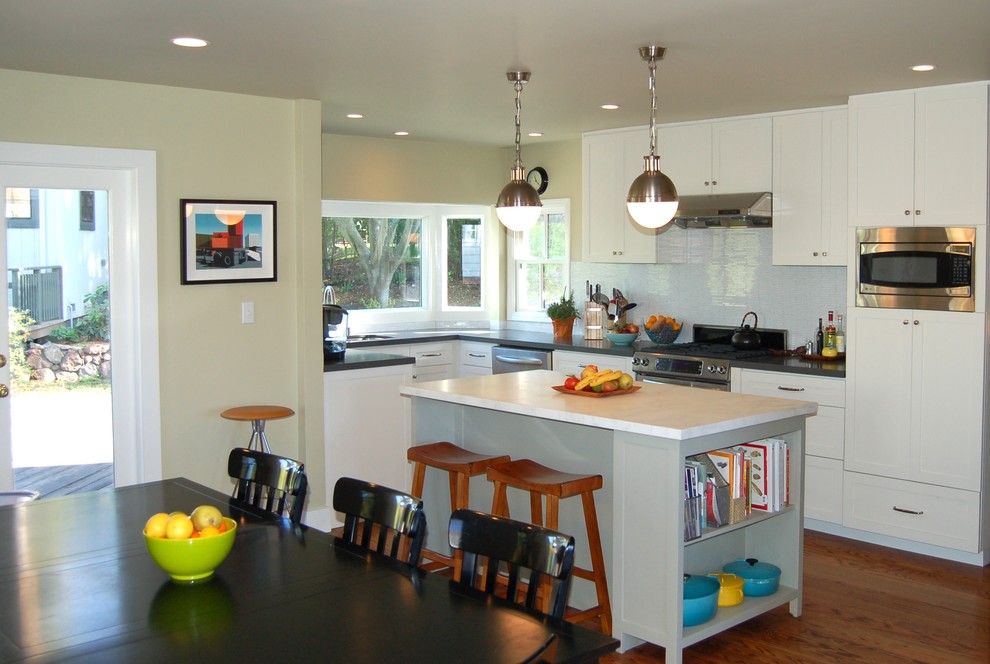 Example of a medium tone wood floor eat-in kitchen design in San Francisco with an undermount sink, white cabinets, glass tile backsplash and stainless steel appliances