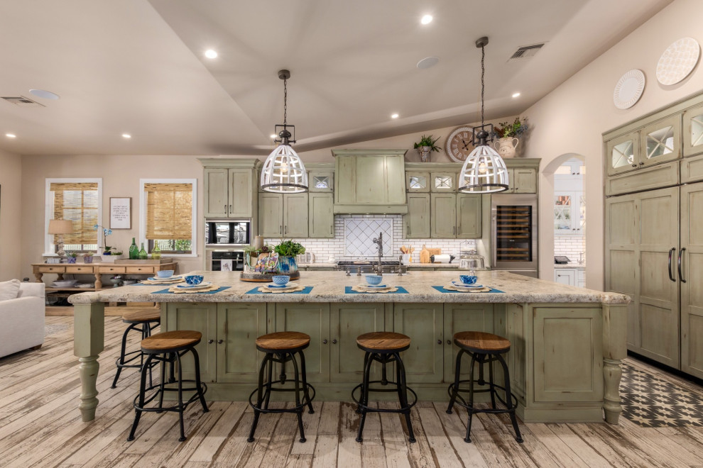 Example of a country l-shaped light wood floor, beige floor and vaulted ceiling kitchen design in Phoenix with a farmhouse sink, green cabinets, granite countertops, white backsplash, stainless steel appliances, an island, recessed-panel cabinets, subway tile backsplash and gray countertops