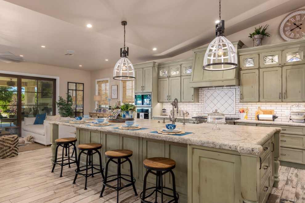 Example of a country kitchen design in Phoenix with a farmhouse sink, green cabinets, granite countertops, white backsplash, stainless steel appliances and an island
