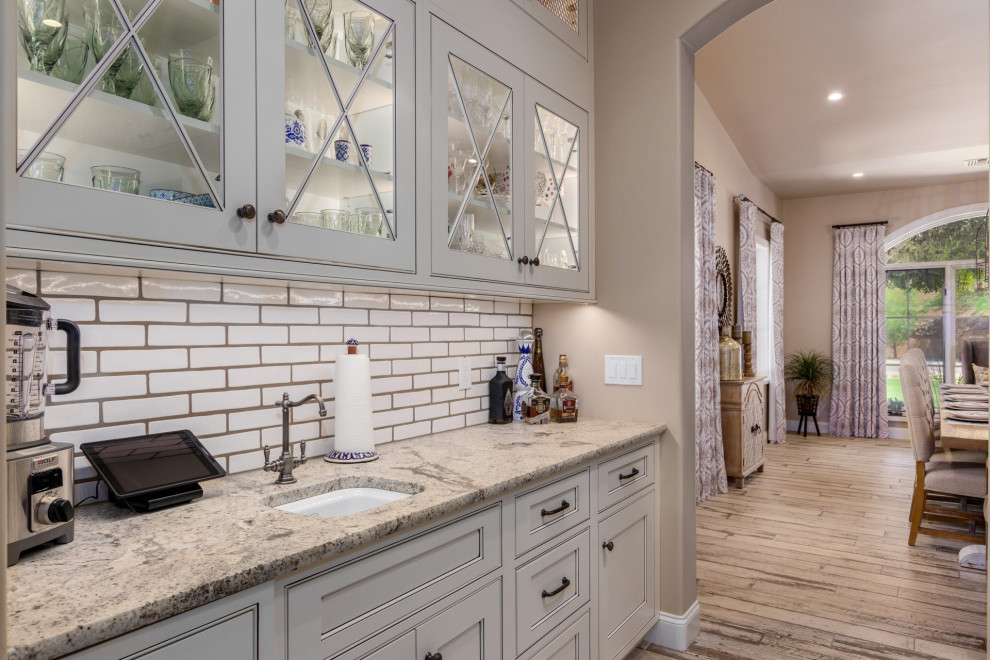Lantlig inredning av ett kök, med en undermonterad diskho, vita skåp, granitbänkskiva, vitt stänkskydd, rostfria vitvaror och en köksö