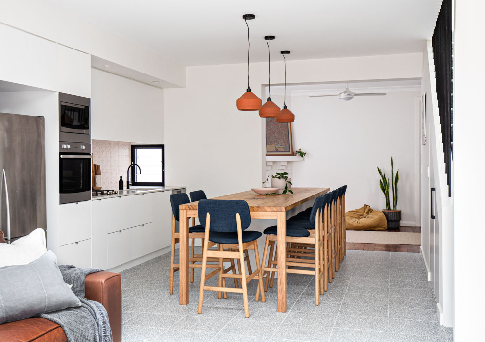 Modern inredning av ett litet brun brunt kök, med en undermonterad diskho, vita skåp, träbänkskiva, rosa stänkskydd, stänkskydd i keramik, rostfria vitvaror, terrazzogolv, en köksö och grått golv