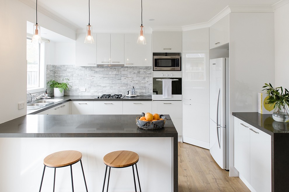 This is an example of a large modern u-shaped kitchen in Melbourne with a double-bowl sink, open cabinets, white cabinets, composite countertops, grey splashback, cement tile splashback, white appliances, light hardwood flooring, an island and grey worktops.