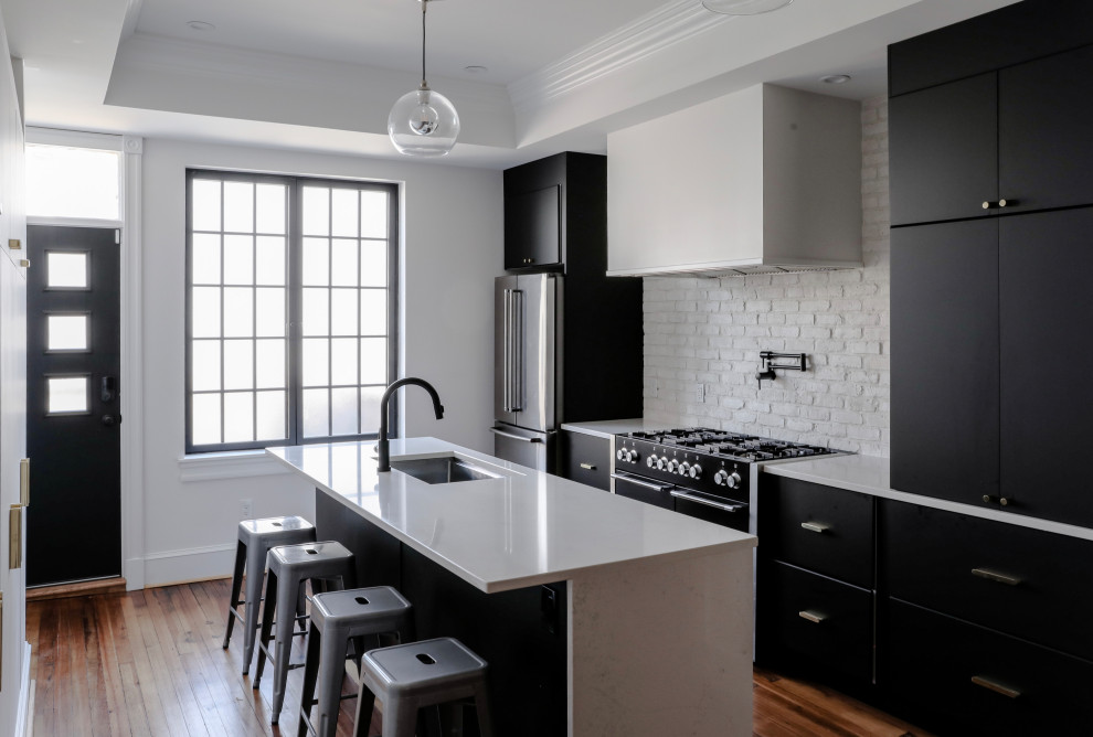 Bild på ett mellanstort funkis vit vitt kök, med en undermonterad diskho, släta luckor, svarta skåp, bänkskiva i kvarts, vitt stänkskydd, stänkskydd i tegel, rostfria vitvaror, mellanmörkt trägolv, en köksö och brunt golv