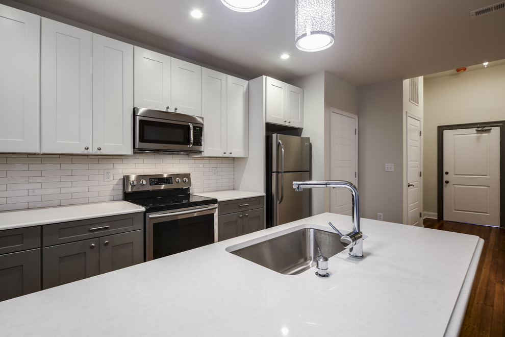 Example of a small minimalist galley medium tone wood floor and brown floor eat-in kitchen design in Baltimore with an undermount sink, shaker cabinets, white cabinets, quartz countertops, white backsplash, subway tile backsplash, stainless steel appliances and an island