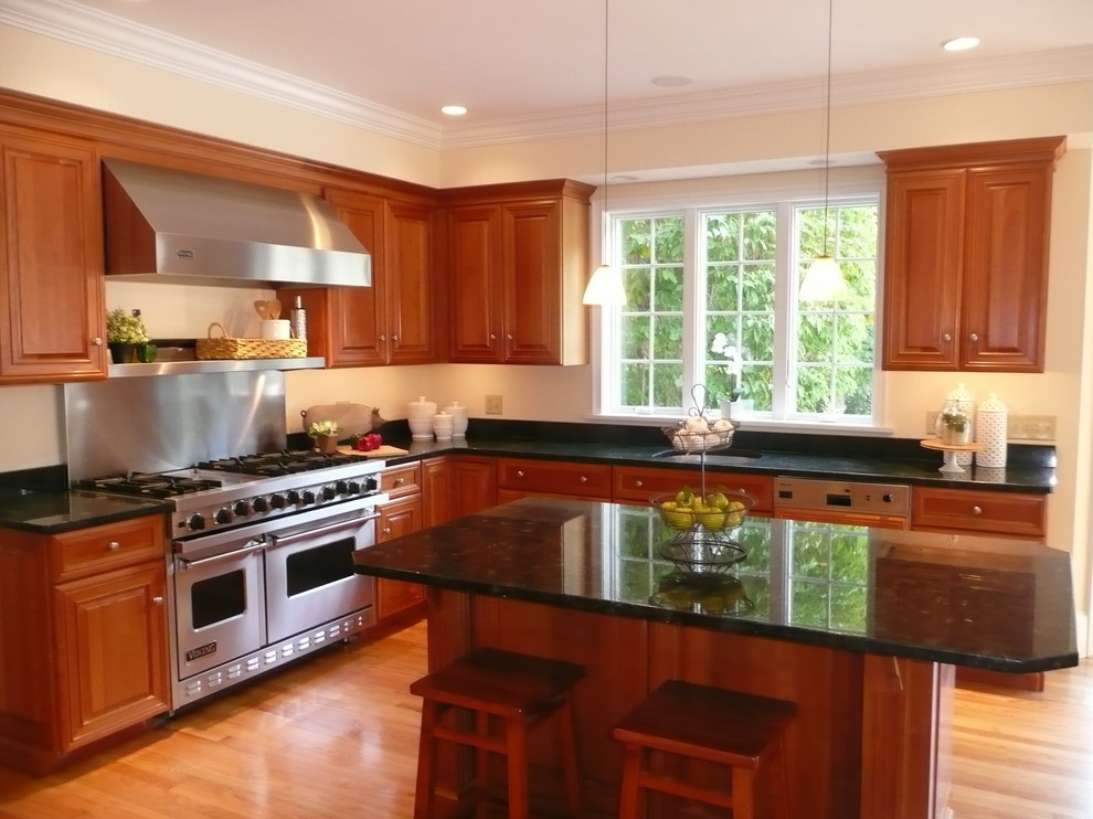 Photo of a large traditional l-shaped kitchen/diner in Boston with a submerged sink, raised-panel cabinets, medium wood cabinets, granite worktops, stainless steel appliances, light hardwood flooring and an island.