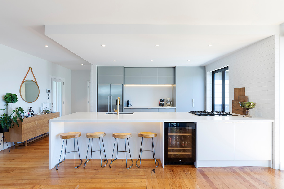This is an example of a modern galley open plan kitchen in Hamilton with a submerged sink, flat-panel cabinets, grey cabinets, white splashback, medium hardwood flooring, a breakfast bar and brown floors.