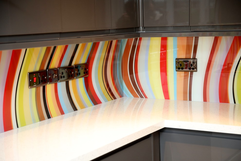 Modelo de cocina contemporánea extra grande abierta con armarios con paneles lisos, puertas de armario grises, salpicadero multicolor, salpicadero de vidrio templado y dos o más islas