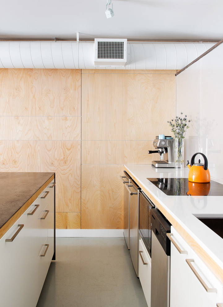 Cette photo montre une cuisine parallèle industrielle avec un évier encastré, un placard à porte plane, des portes de placard blanches et un électroménager en acier inoxydable.