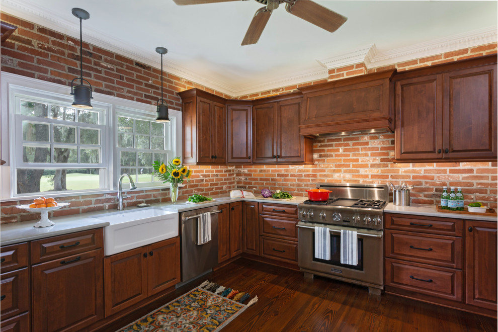 Design ideas for a classic u-shaped enclosed kitchen in Charleston with a belfast sink, raised-panel cabinets, dark wood cabinets, brick splashback, stainless steel appliances, dark hardwood flooring and white worktops.