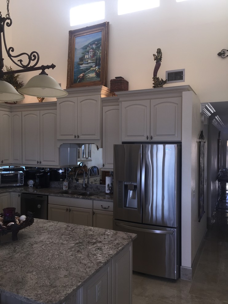 Medium sized eclectic l-shaped open plan kitchen in Miami with a submerged sink, raised-panel cabinets, white cabinets, granite worktops, mirror splashback, stainless steel appliances, porcelain flooring, an island and beige floors.