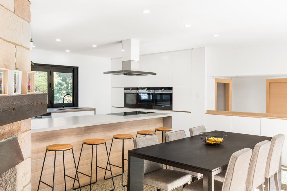 This is an example of a large contemporary galley kitchen/diner in Sydney with a submerged sink, white cabinets, composite countertops, white splashback, window splashback, black appliances, concrete flooring, an island, grey floors and white worktops.