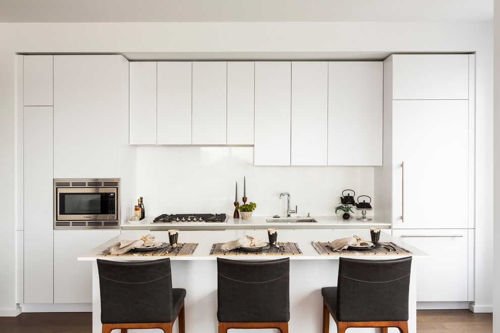 Immagine di una cucina contemporanea con lavello sottopiano, ante lisce, ante bianche, paraspruzzi bianco, elettrodomestici in acciaio inossidabile, parquet scuro, pavimento marrone e top bianco