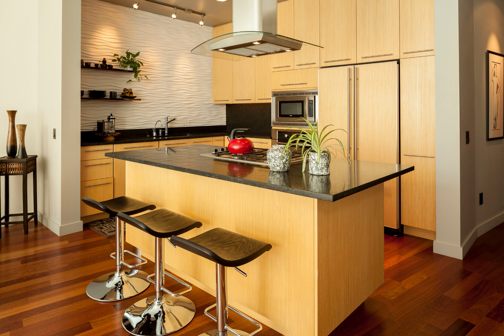 Example of a mid-sized trendy l-shaped medium tone wood floor eat-in kitchen design in Portland with flat-panel cabinets, light wood cabinets, laminate countertops, white backsplash, an island, a single-bowl sink, glass tile backsplash and paneled appliances