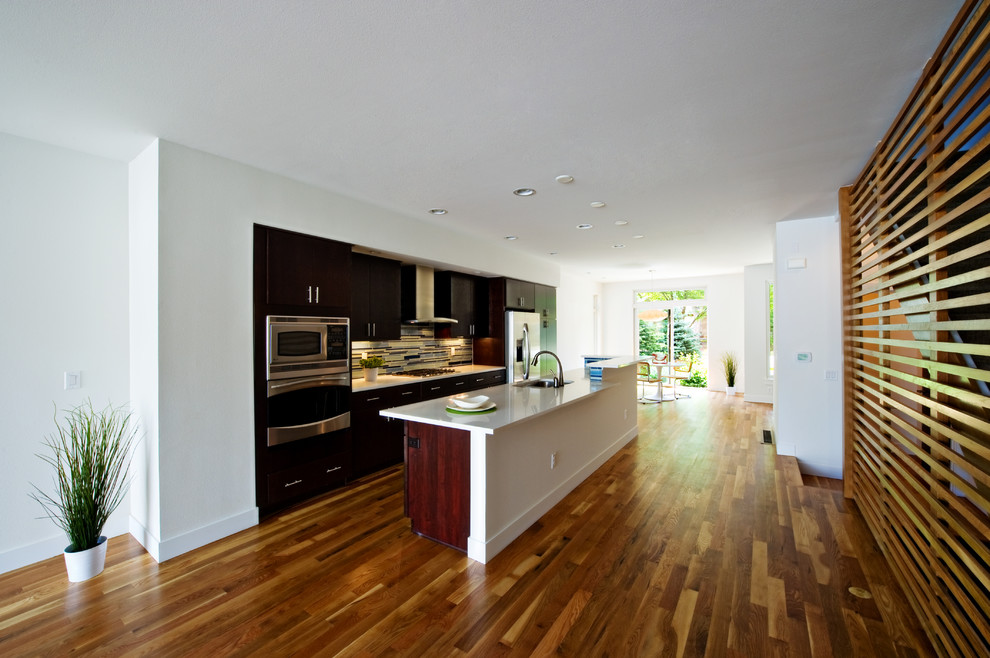 Bild på ett funkis kök, med släta luckor, skåp i mörkt trä, flerfärgad stänkskydd och rostfria vitvaror