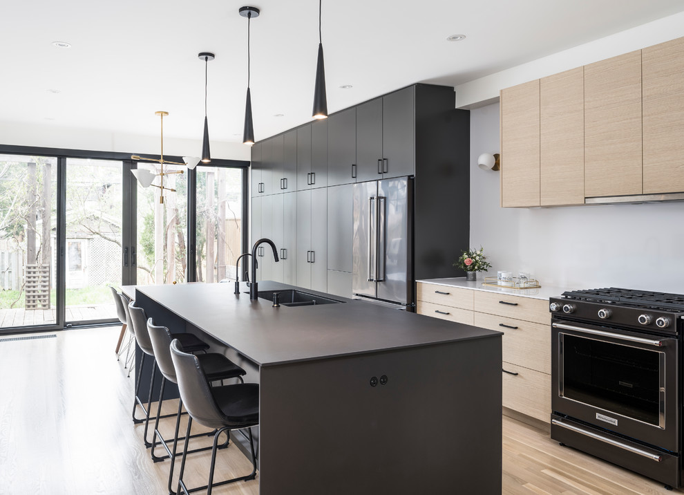 Immagine di una cucina contemporanea con lavello sottopiano, ante lisce, ante in legno chiaro, elettrodomestici neri, pavimento in legno massello medio, pavimento marrone e top bianco