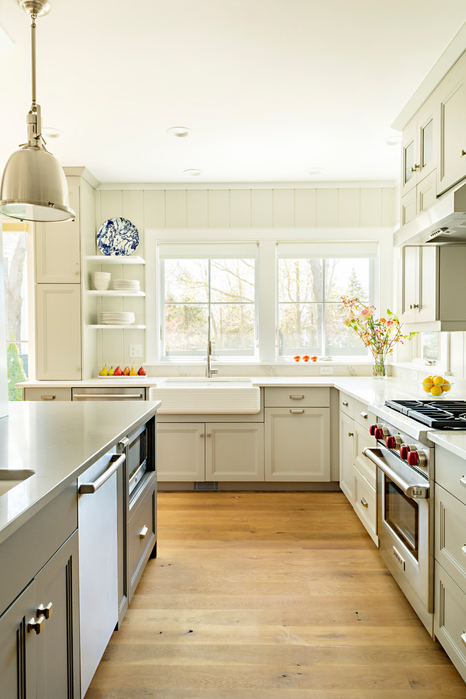 ボストンにある広いカントリー風のおしゃれなアイランドキッチン (シェーカースタイル扉のキャビネット、ベージュのキャビネット、ステンレスカウンター、白いキッチンパネル、シルバーの調理設備、無垢フローリング、白いキッチンカウンター) の写真