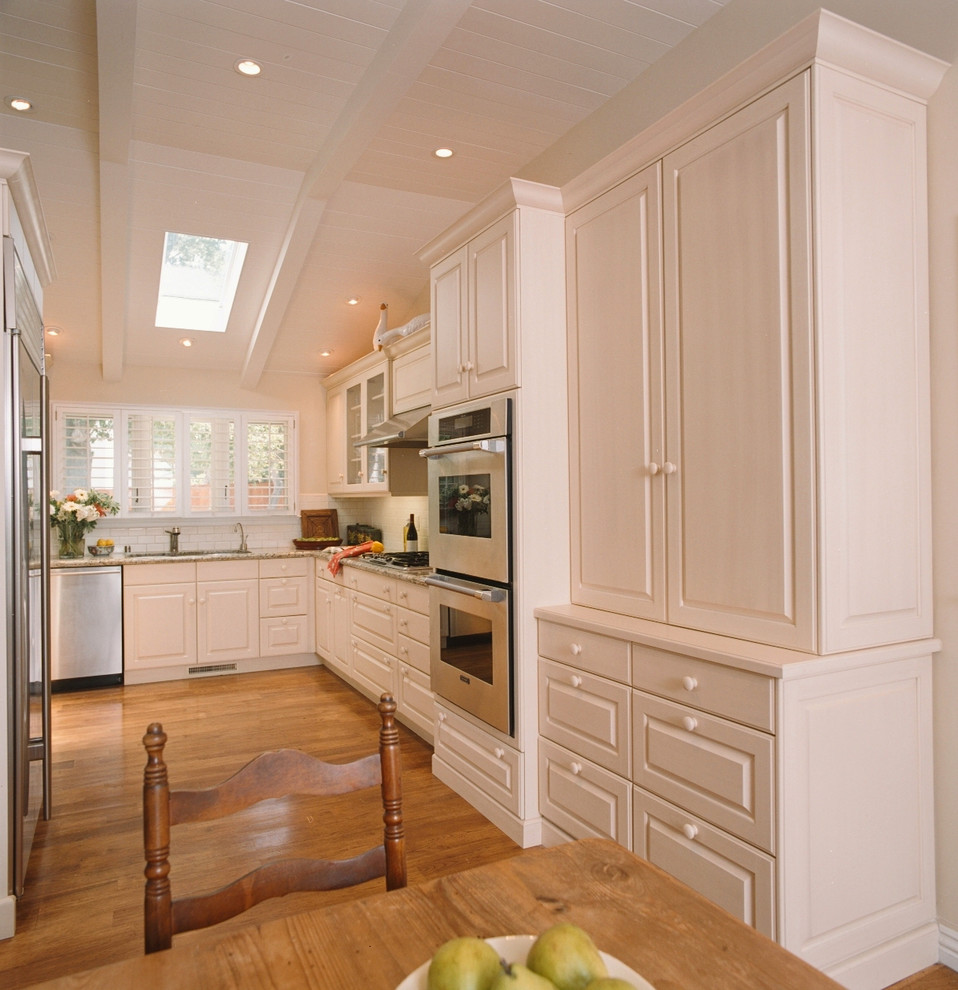 Exempel på ett klassiskt kök, med en undermonterad diskho, luckor med upphöjd panel, vita skåp, granitbänkskiva, vitt stänkskydd, stänkskydd i tunnelbanekakel och rostfria vitvaror