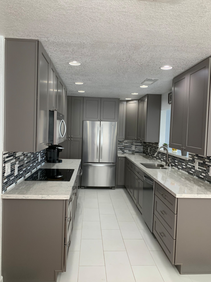 Photo of a medium sized contemporary l-shaped kitchen/diner in Sacramento with a submerged sink, shaker cabinets, grey cabinets, engineered stone countertops, blue splashback, glass tiled splashback, stainless steel appliances, porcelain flooring, no island, white floors and white worktops.