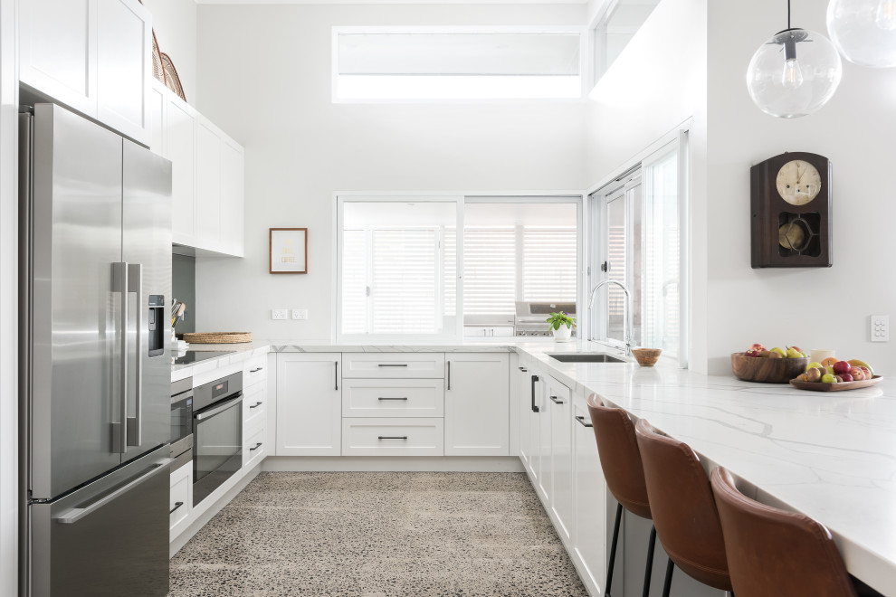Idéer för ett modernt vit u-kök, med en undermonterad diskho, skåp i shakerstil, vita skåp, rostfria vitvaror, en halv köksö och grått golv