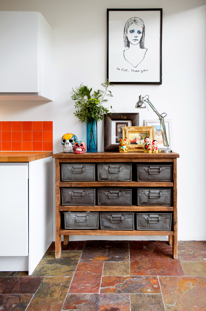 Inspiration for a mid-sized eclectic slate floor kitchen remodel in London with a farmhouse sink, flat-panel cabinets, white cabinets, wood countertops, orange backsplash, ceramic backsplash, stainless steel appliances and an island