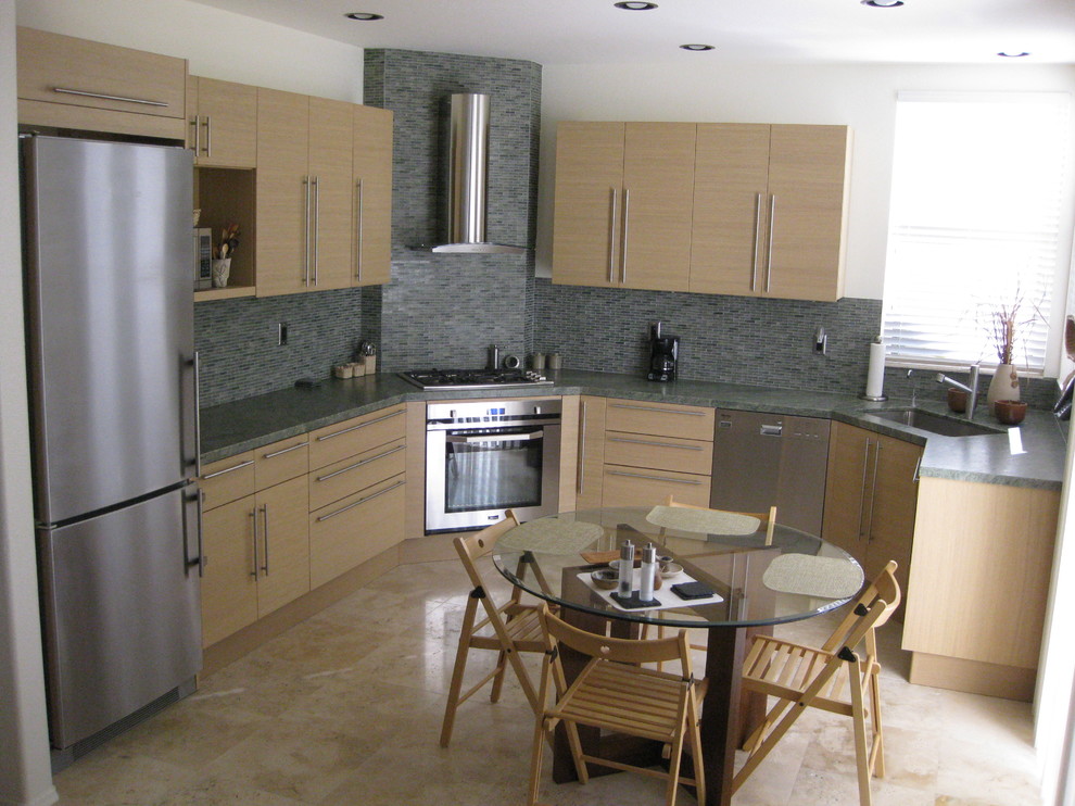 This is an example of a medium sized contemporary u-shaped kitchen/diner in San Diego with a submerged sink, flat-panel cabinets, light wood cabinets, granite worktops, green splashback, glass tiled splashback, stainless steel appliances and travertine flooring.