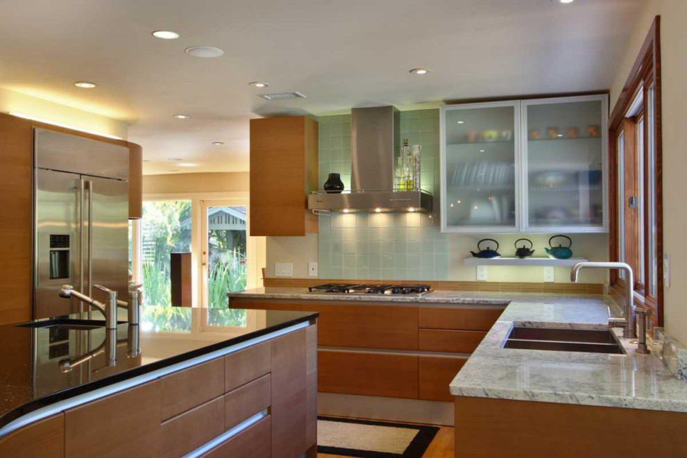 Foto på ett stort 60 tals grå kök, med en undermonterad diskho, släta luckor, skåp i mellenmörkt trä, bänkskiva i glas, grönt stänkskydd, stänkskydd i glaskakel, rostfria vitvaror, mellanmörkt trägolv, en köksö och turkost golv