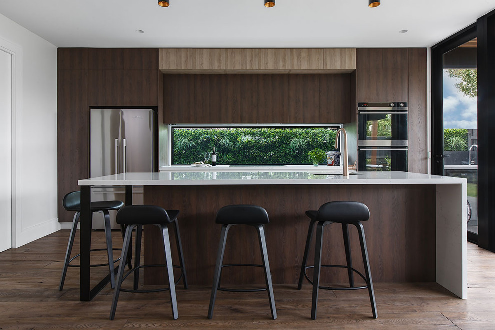 Zweizeilige Moderne Küche mit Unterbauwaschbecken, flächenbündigen Schrankfronten, dunklen Holzschränken, Rückwand-Fenster, Küchengeräten aus Edelstahl, dunklem Holzboden, Kücheninsel, braunem Boden und weißer Arbeitsplatte in Melbourne