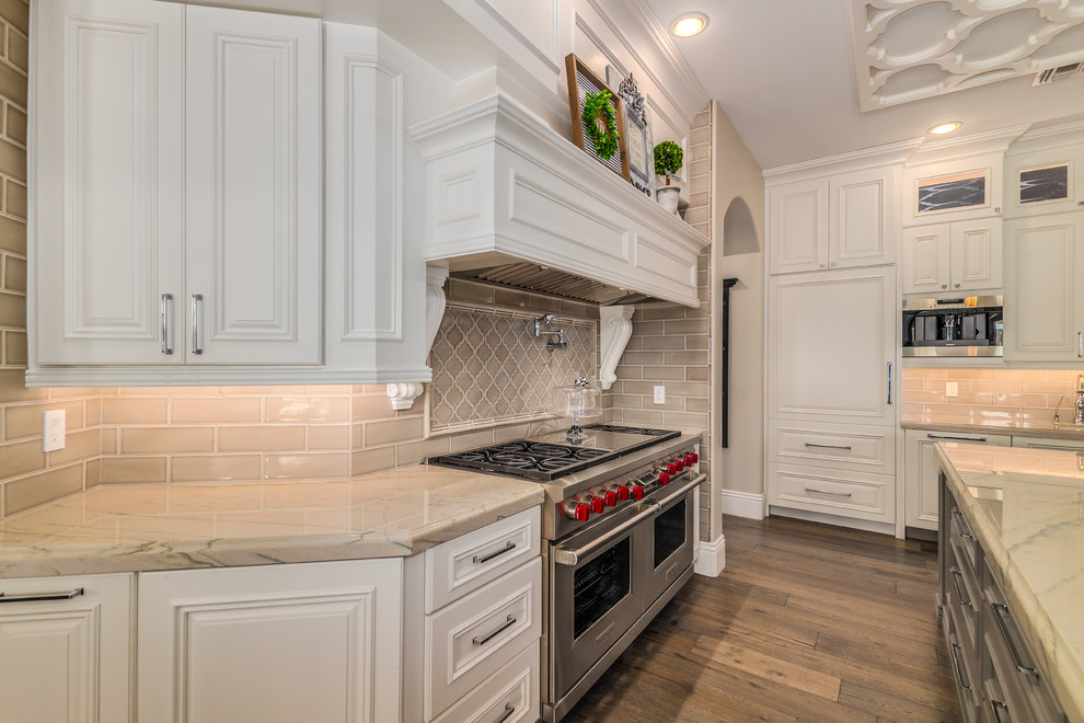 Exempel på ett stort klassiskt flerfärgad flerfärgat kök, med en undermonterad diskho, luckor med profilerade fronter, vita skåp, marmorbänkskiva, grått stänkskydd, stänkskydd i keramik, integrerade vitvaror, mellanmörkt trägolv, en köksö och brunt golv