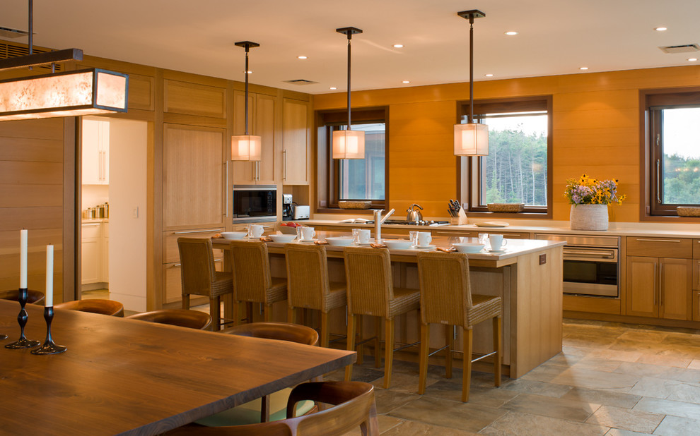 На фото: угловая кухня в современном стиле с обеденным столом, фасадами цвета дерева среднего тона и техникой под мебельный фасад