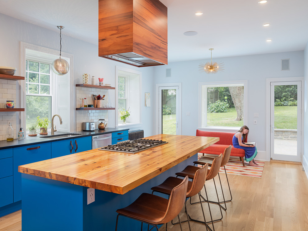 Contemporary galley kitchen in Philadelphia with a submerged sink, flat-panel cabinets, blue cabinets, white splashback, metro tiled splashback, stainless steel appliances, light hardwood flooring and an island.