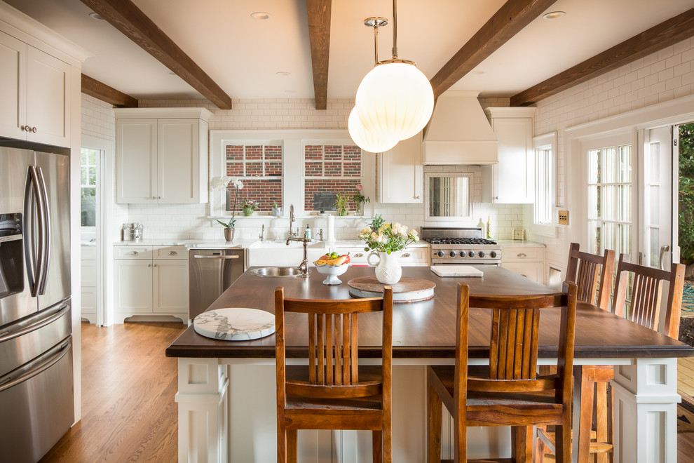 Foto på ett vintage kök, med skåp i shakerstil, vita skåp, vitt stänkskydd, stänkskydd i tunnelbanekakel, rostfria vitvaror, mellanmörkt trägolv, en köksö och brunt golv