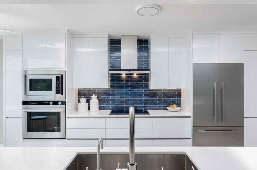 Mid-sized trendy galley ceramic tile and gray floor enclosed kitchen photo in Other with an undermount sink, flat-panel cabinets, white cabinets, quartz countertops, blue backsplash, stainless steel appliances and white countertops