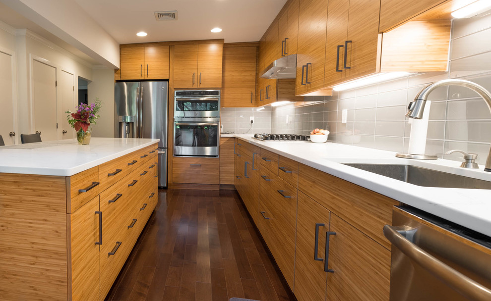 This is an example of a medium sized contemporary l-shaped kitchen/diner in Philadelphia with a built-in sink, flat-panel cabinets, medium wood cabinets, engineered stone countertops, grey splashback, porcelain splashback, stainless steel appliances, medium hardwood flooring, an island and brown floors.