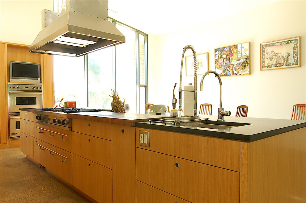 Example of a mid-sized trendy galley concrete floor open concept kitchen design in Austin with an undermount sink, flat-panel cabinets, light wood cabinets, granite countertops, brown backsplash, stainless steel appliances and an island
