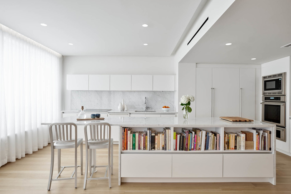 Idéer för att renovera ett funkis l-kök, med en undermonterad diskho, släta luckor, vita skåp, vitt stänkskydd, rostfria vitvaror, ljust trägolv, en köksö och beiget golv