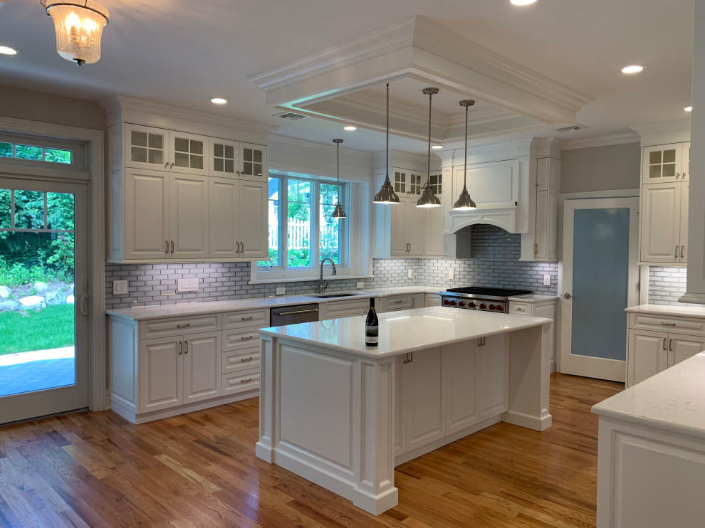 Large traditional l-shaped open plan kitchen in New York with beaded cabinets, white cabinets, grey splashback, metro tiled splashback, medium hardwood flooring, an island, brown floors and yellow worktops.