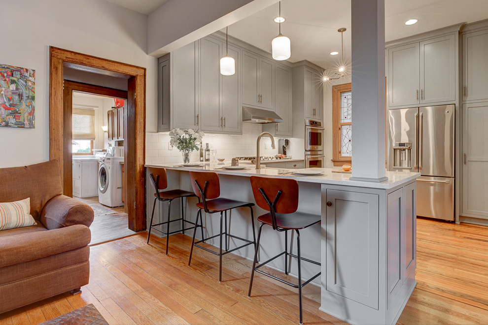 Eat-in kitchen - mid-sized contemporary l-shaped light wood floor eat-in kitchen idea in Los Angeles with a farmhouse sink, beaded inset cabinets, gray cabinets, quartzite countertops, white backsplash, subway tile backsplash, stainless steel appliances and a peninsula