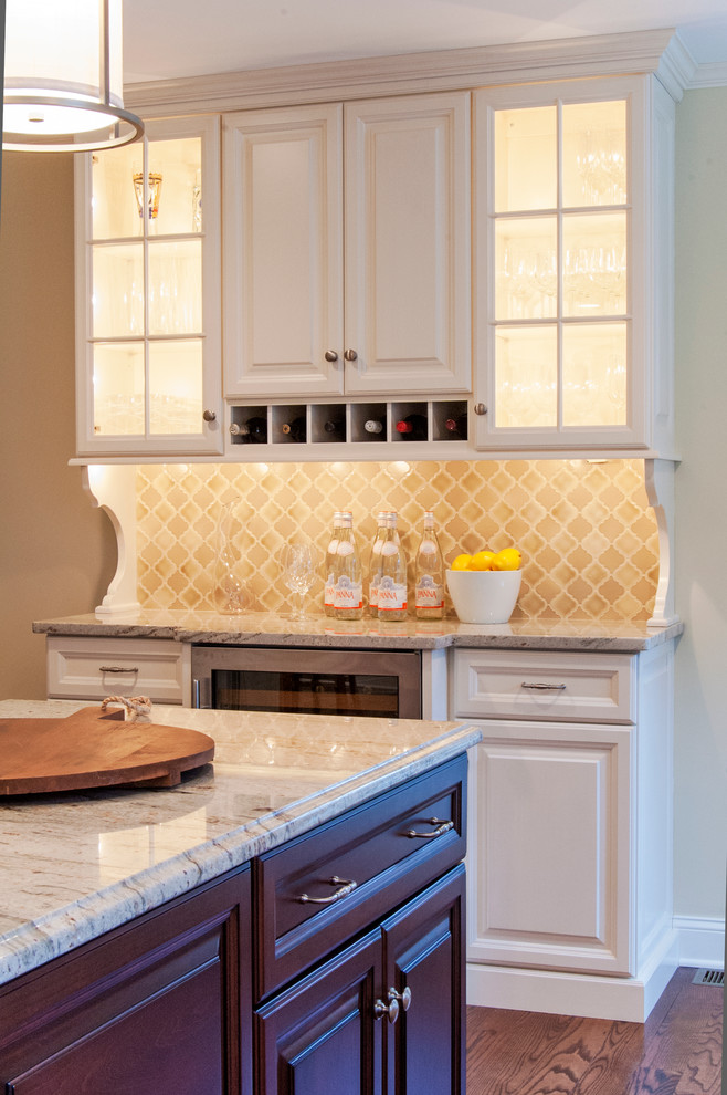 Cette photo montre une cuisine chic avec des portes de placard blanches, un plan de travail en granite, une crédence beige, une crédence en céramique, un électroménager en acier inoxydable, un sol en bois brun et îlot.