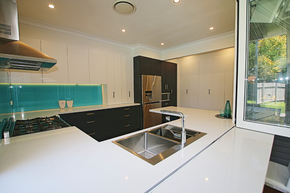Example of a mid-sized trendy u-shaped vinyl floor eat-in kitchen design in Sydney with a drop-in sink, flat-panel cabinets, blue cabinets, quartz countertops, blue backsplash, glass sheet backsplash, stainless steel appliances and a peninsula