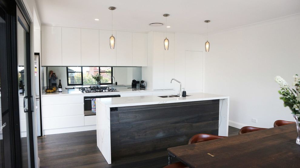 Mid-sized minimalist galley dark wood floor and gray floor eat-in kitchen photo in Sydney with an undermount sink, flat-panel cabinets, white cabinets, quartz countertops, white backsplash, glass sheet backsplash, stainless steel appliances, an island and white countertops