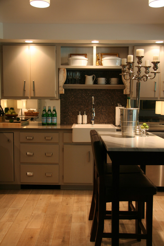 Bild på ett mellanstort lantligt u-kök, med en rustik diskho, släta luckor, grå skåp, bänkskiva i kvartsit, spegel som stänkskydd, rostfria vitvaror och ljust trägolv