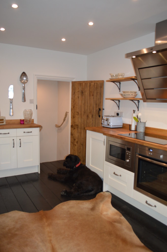 Exemple d'une petite cuisine américaine chic avec un évier de ferme, un placard à porte shaker, un plan de travail en bois, un électroménager en acier inoxydable et parquet peint.