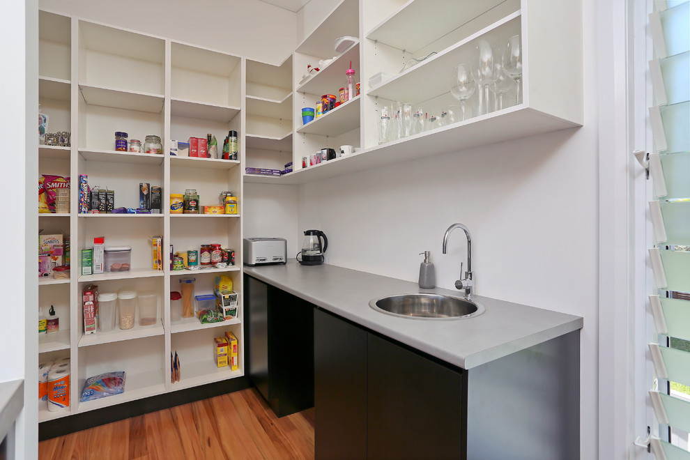 This is an example of a large contemporary galley kitchen pantry in Sydney with a built-in sink, flat-panel cabinets, light wood cabinets, engineered stone countertops, black splashback, glass sheet splashback, stainless steel appliances, light hardwood flooring, a breakfast bar and yellow floors.