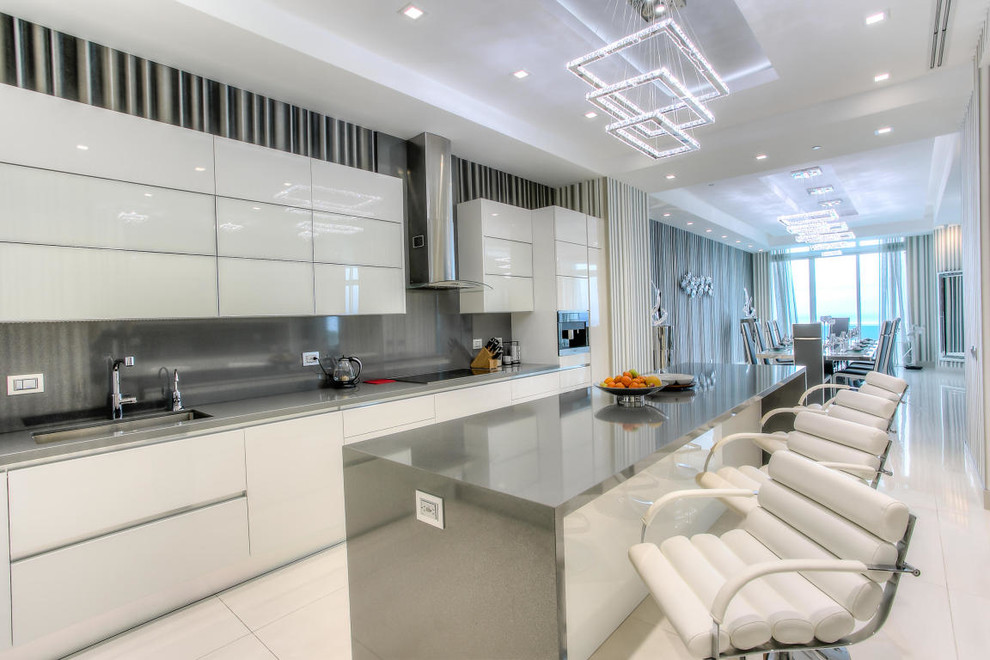 Photo of an expansive contemporary l-shaped kitchen/diner in Miami with a submerged sink, flat-panel cabinets, stainless steel worktops, metallic splashback, metal splashback, stainless steel appliances, porcelain flooring, an island and white cabinets.