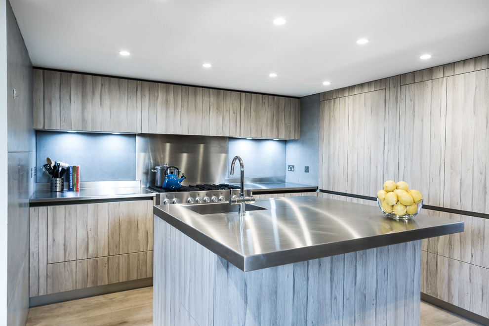 Photo of a medium sized contemporary l-shaped open plan kitchen in London with a built-in sink, flat-panel cabinets, stainless steel worktops, grey splashback, cement tile splashback, integrated appliances, light hardwood flooring and a breakfast bar.